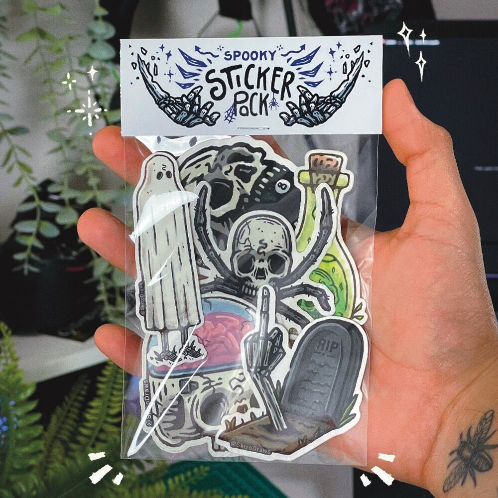 Dłoń trzymająca pakiet naklejek z upiornymi rysunkami i nagłówkiem „SPOOKY STICKER PACK” na tle roślin