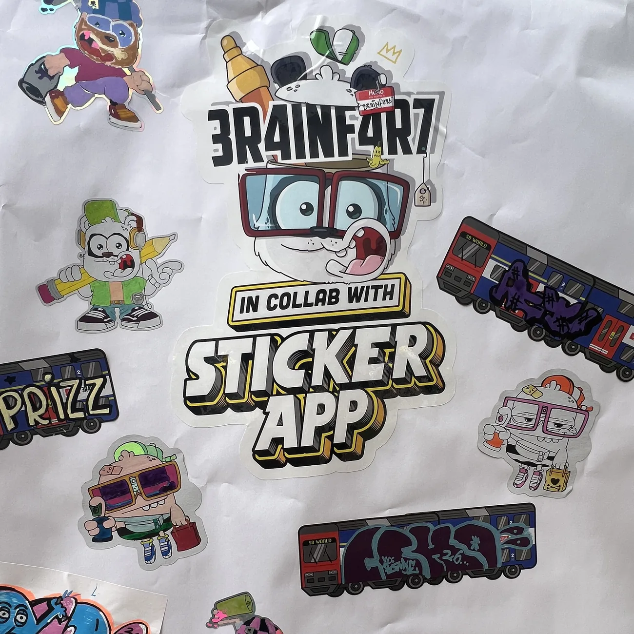 Ściana pokryta ręcznie pokolorowanymi naklejkami wycinanymi do kształtu Brainfart x StickerApp i etykietami z pociągiem S8 World z tagami graffiti
