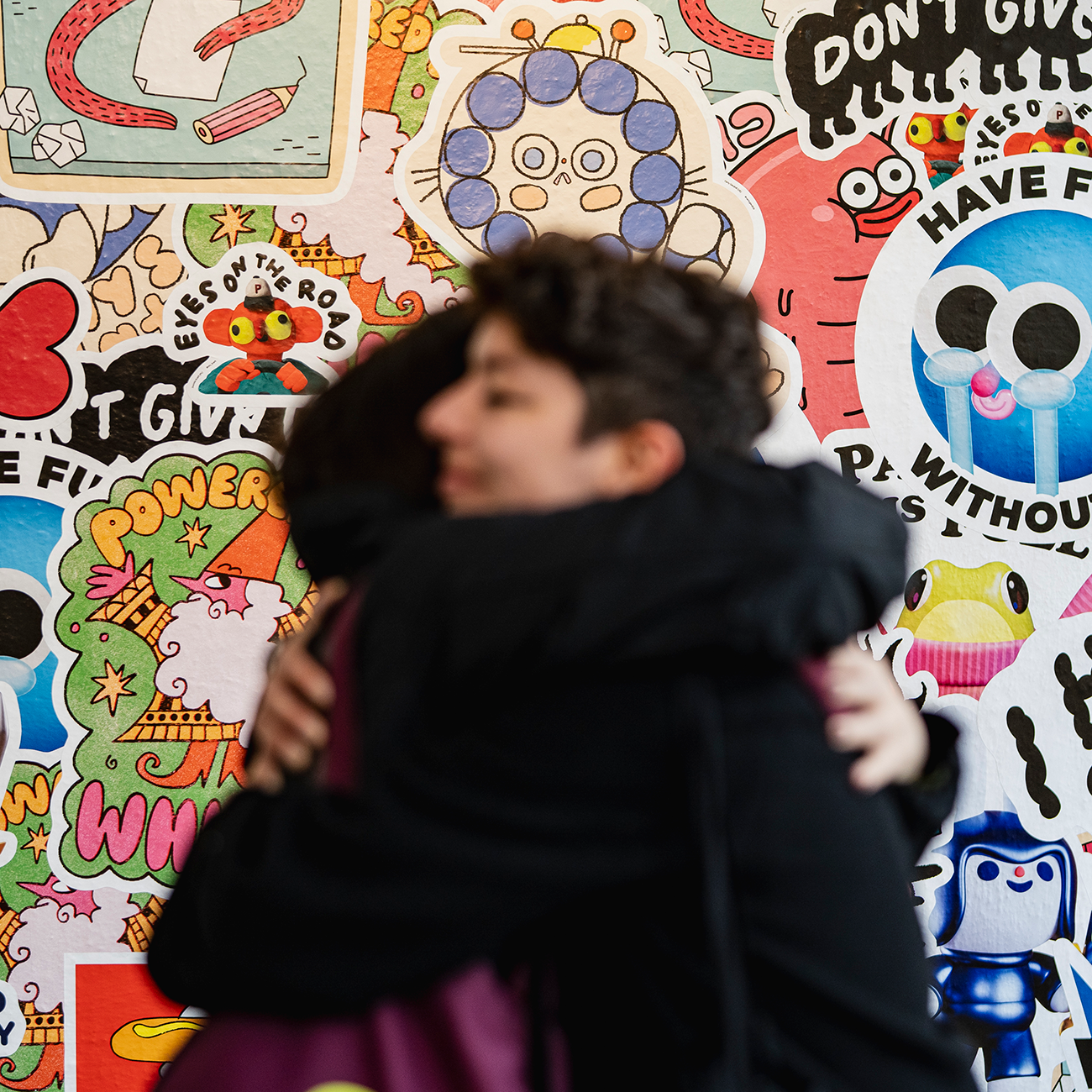 Two people hugging in front of a wall covered in wall stickers in various shapes and sizes.