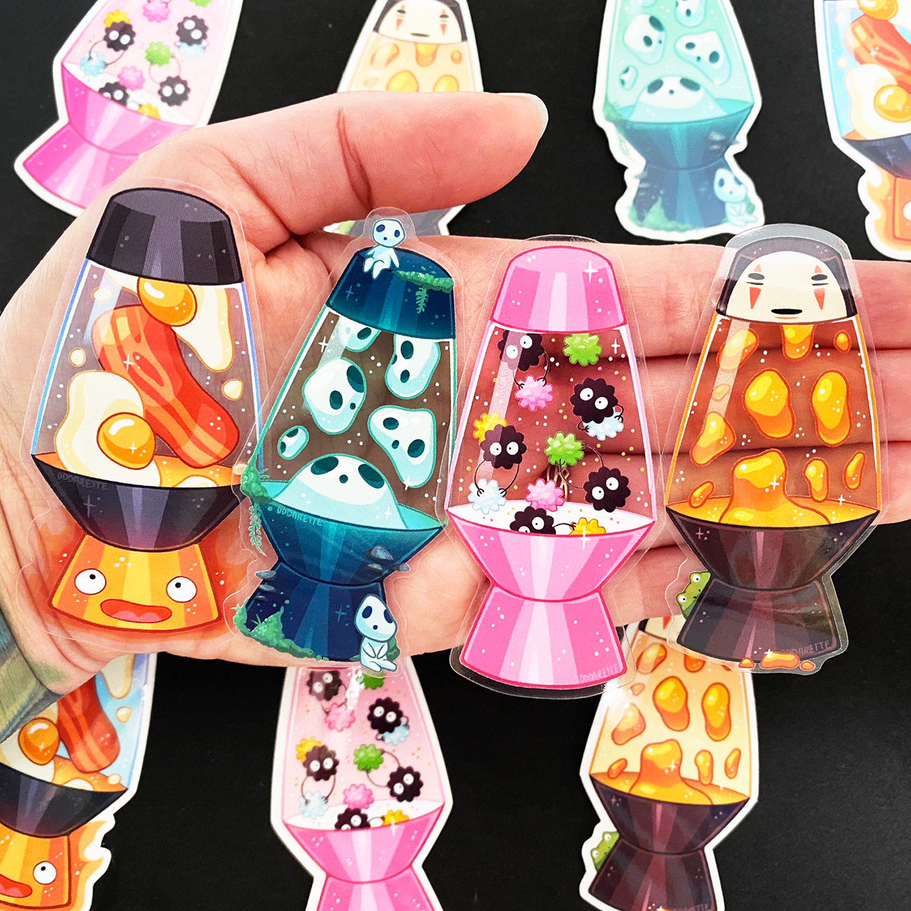 Hand holding colorful transparent lava lamp stickers with various cute designs, including faces and abstract patterns.