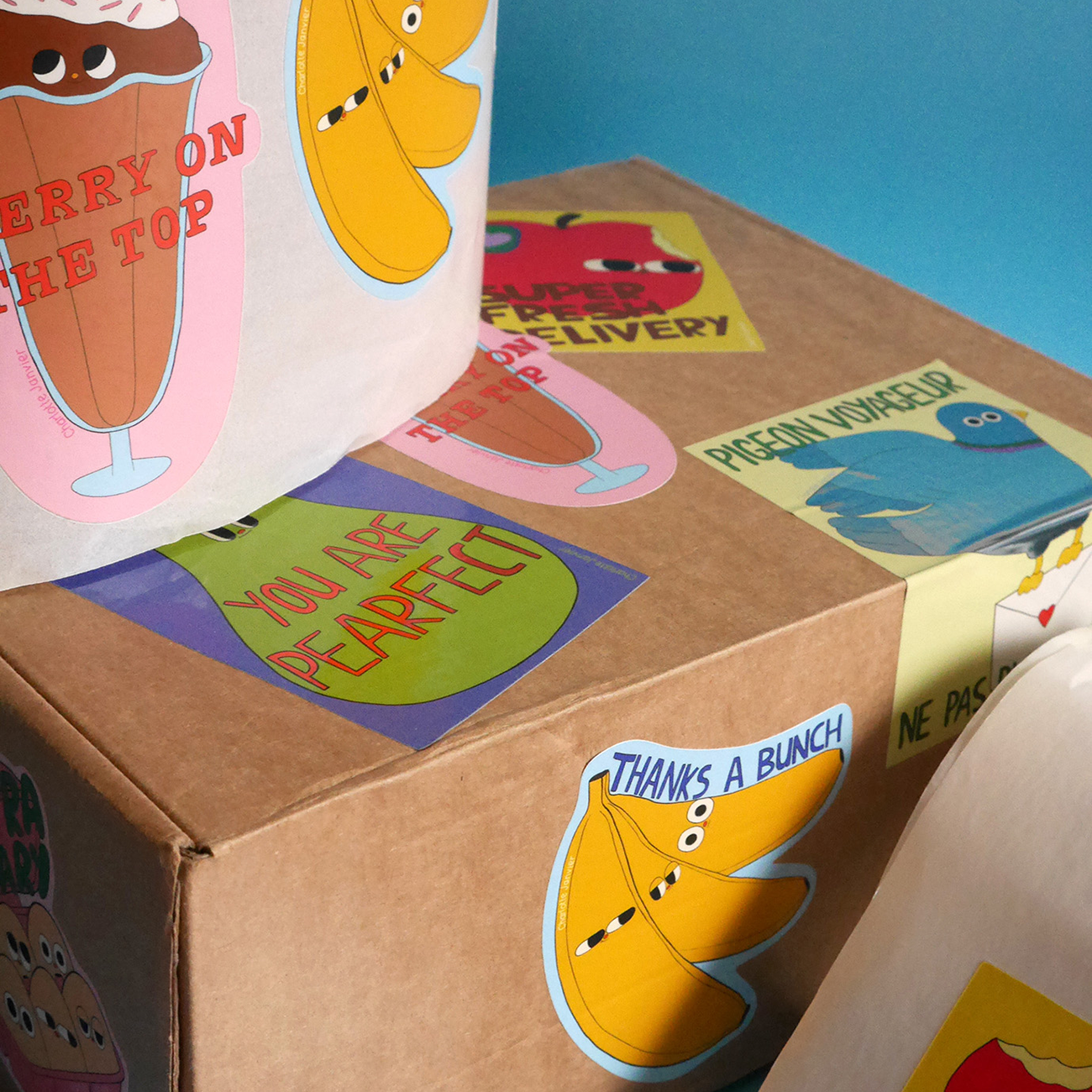 Cardboard boxes with colorful, pun-filled stickers featuring cartoon fruit characters and playful text against a blue background.