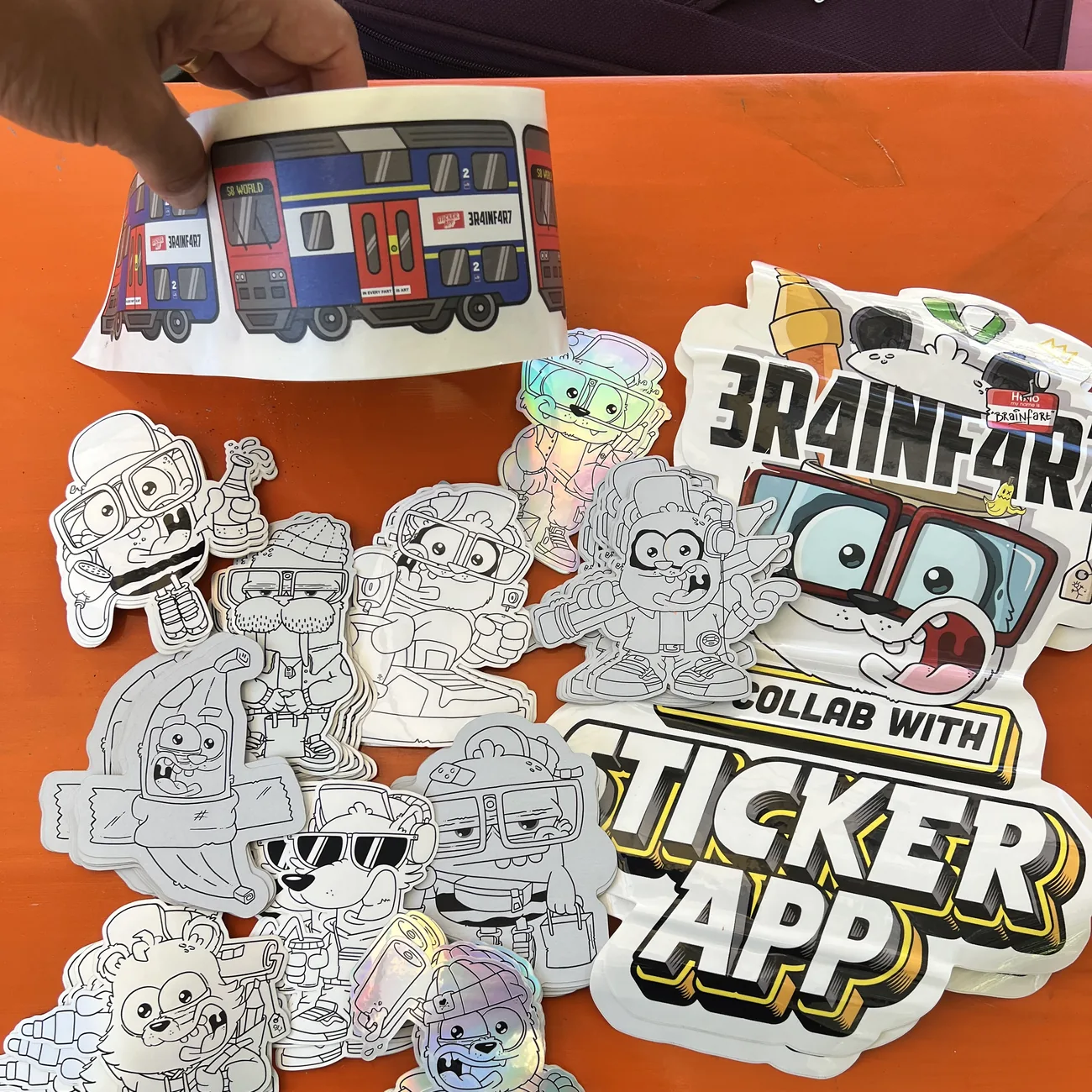 Etykieta z pociągiem S8 World Brainfart x StickerApp z napisem "In every fart is art" trzymana nad czarno-białymi naklejkami wycinanymi do kształtu