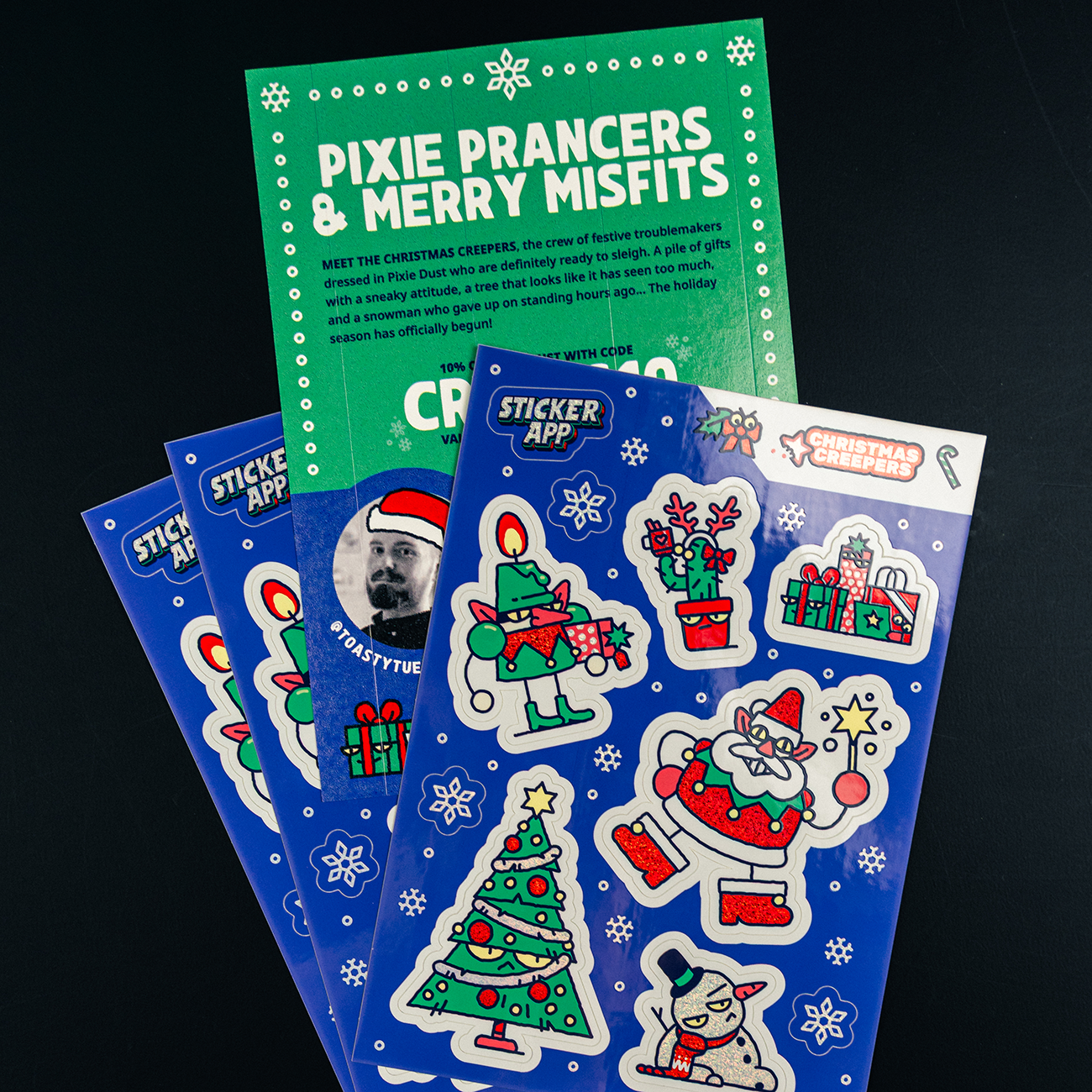 Blue sticker sheets with colorful holiday characters on Pixie Dust, with a text on the back of the sheet saying "Pixie Prancers & Merry Misfits"
