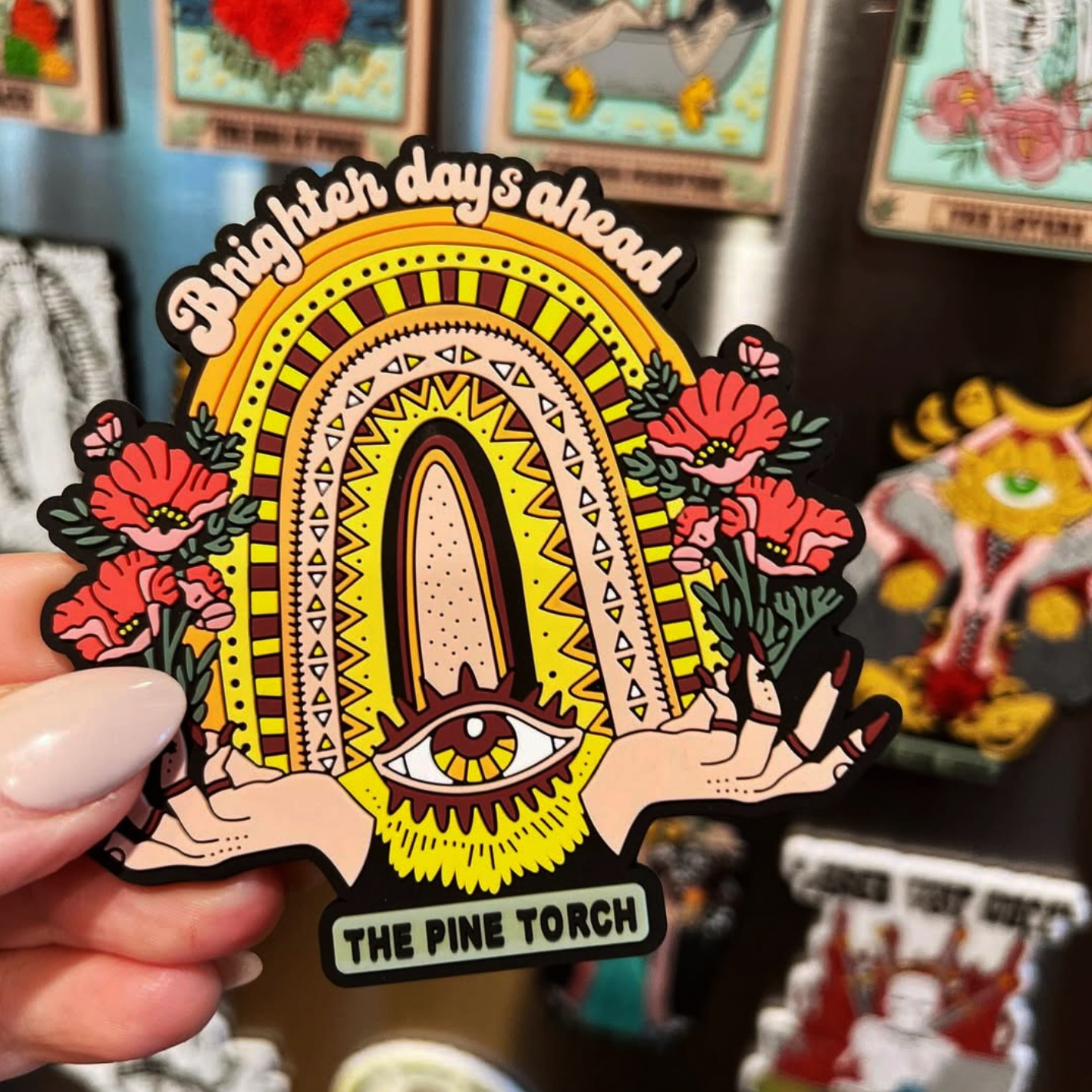 Colorful die-cut vinyl sticker held with the text "Brighter days ahead" held in front of a wall of art