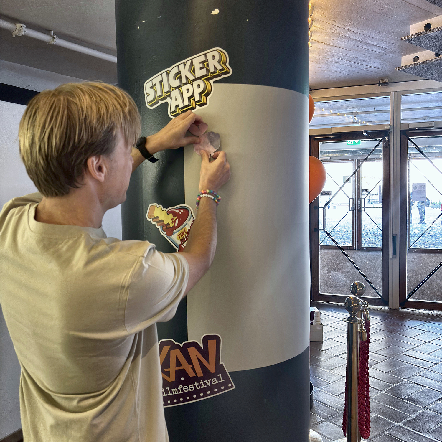 Mężczyzna przykleja naklejkę na ścianę naklejek StickerApp owiniętą wokół filaru na KAN Film Festival
