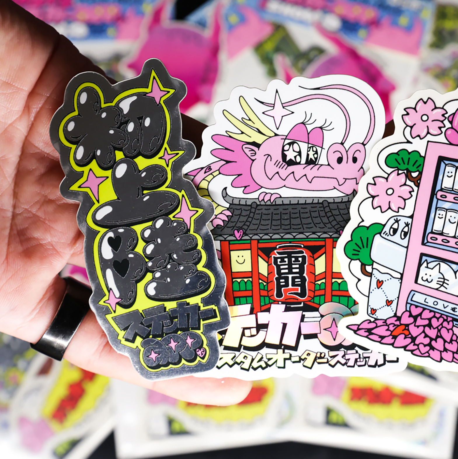 A hand holding colorful, cartoon-style stickers featuring creative designs and Japanese characters in a vibrant, artistic style.
