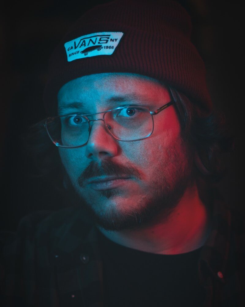 Portret artysty Emila Ronnelina (Bloodstrokes) w okularach i czapce w czerwono-niebieskim świetle